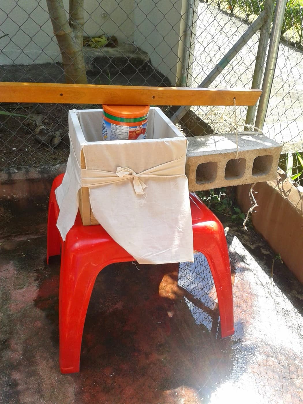 Prensa casera hecha con una silla plástica roja, un cajón y un bloque, en el garaje de la casa